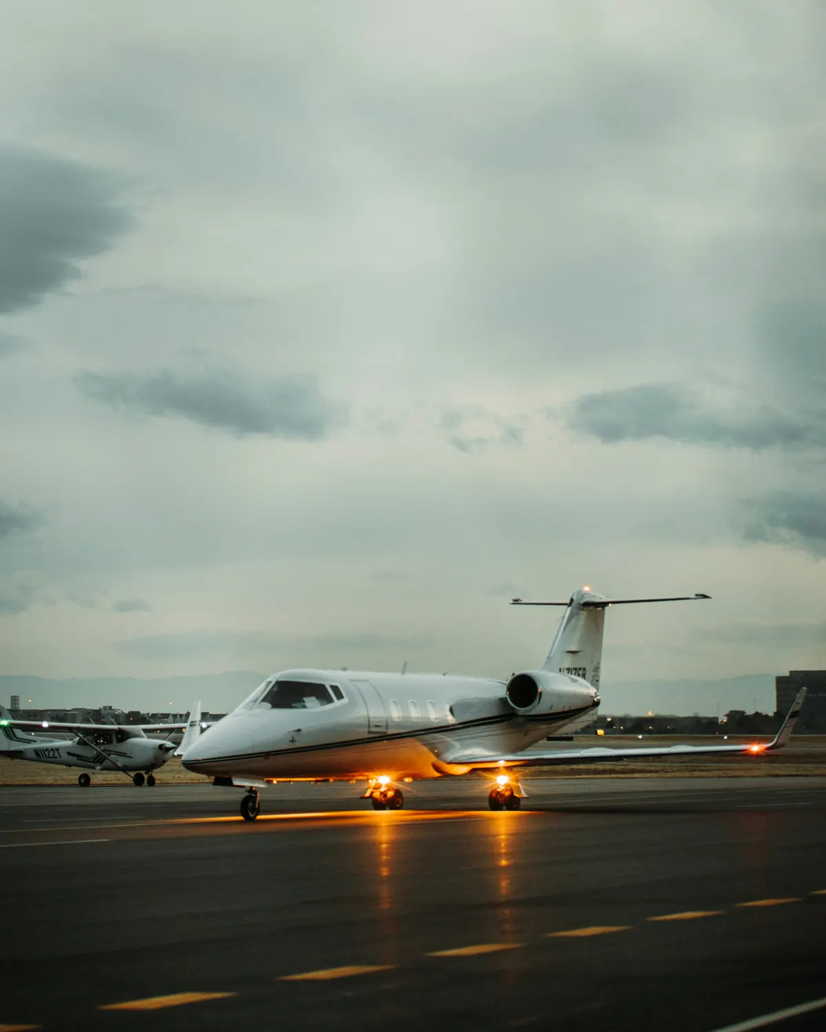 A business jet taxiing on a wet evening with its landing lights on